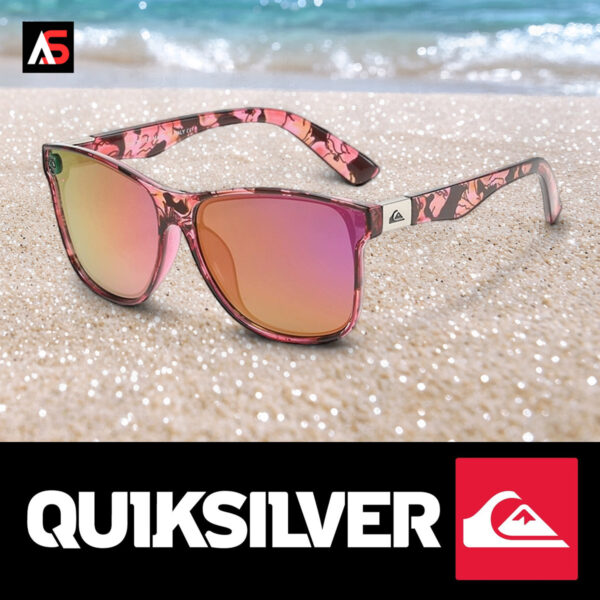 Angled lifestyle view of the Quiksilver 'Flora Pop' Square sunglasses set on a beach with ocean waves in the background, highlighting the pink floral frame and pink mirror lens.