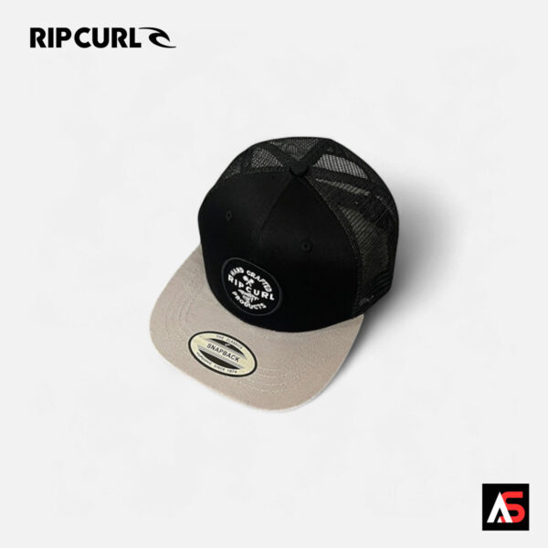 Rip Curl RC103 hand-crafted trucker cap in black and sand, angled studio view showing front panel, mesh back, and curved brim.